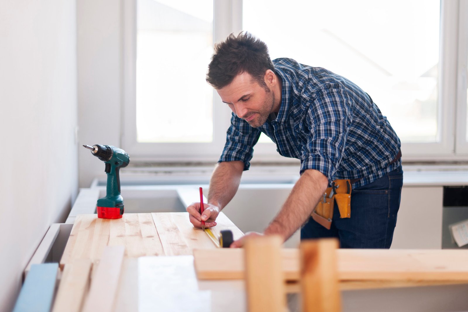 Smiling carpenter measuring wooden planks